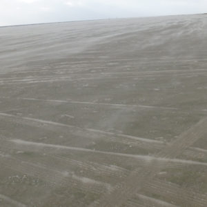 Der Wind fegt den Sand am Strand über die Autospuren