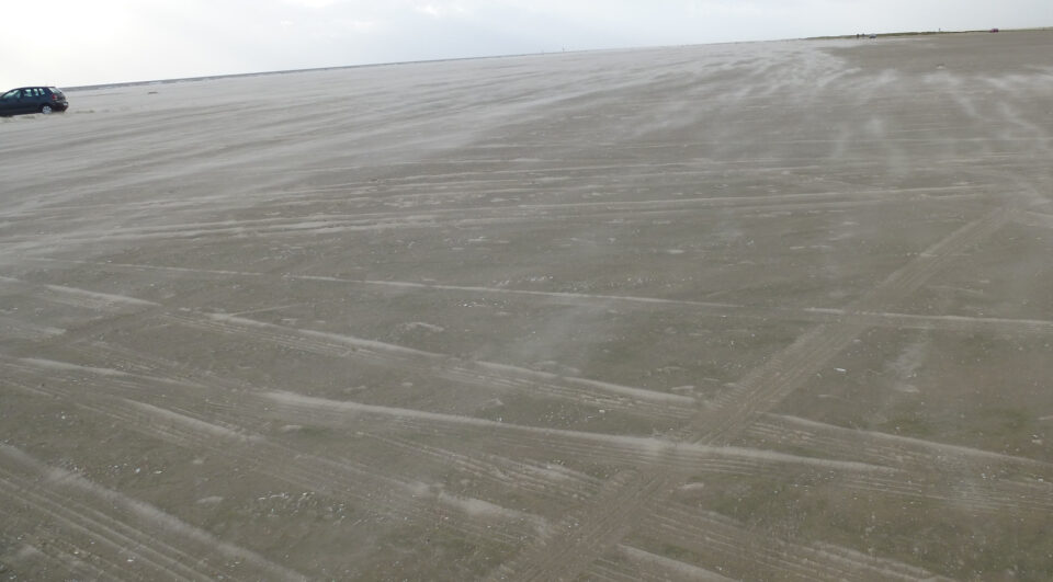 Der Wind fegt den Sand am Strand über die Autospuren
